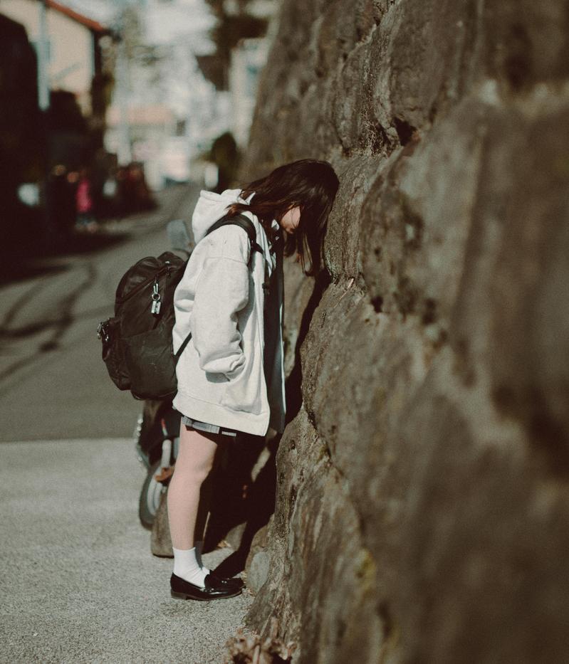 石の壁に向かってうな垂れる女子高生